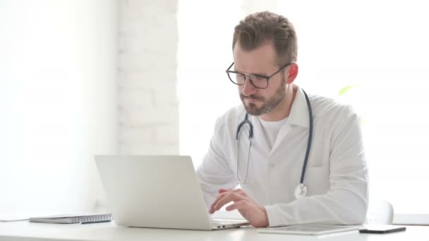 Doctor Looking at Camera while using Laptop in Office — Vídeo de Stock