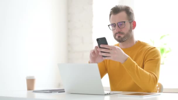 Homem usando Smartphone ao usar Laptop no Office — Vídeo de Stock