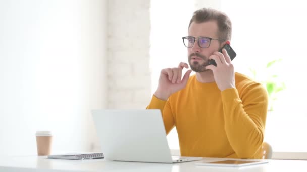 Ο άνθρωπος που μιλά στο τηλέφωνο ενώ χρησιμοποιεί το lap-top στο γραφείο — Αρχείο Βίντεο