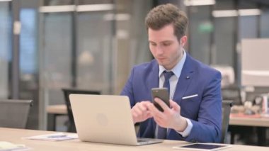 Ofiste dizüstü bilgisayar kullanırken Smartphone kullanan bir işadamı 