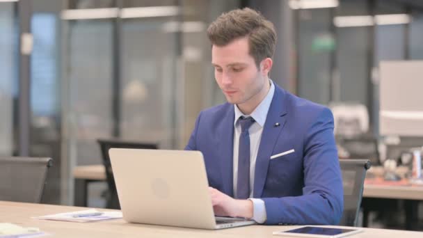 Empresario sonriendo a la cámara mientras usa el ordenador portátil en la oficina — Vídeos de Stock