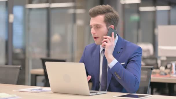 Uomo d'affari arrabbiato che parla al telefono durante l'utilizzo del computer portatile in ufficio — Video Stock
