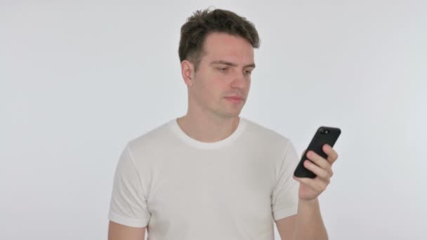 Rozzlobený mladý muž mluví na telefonu na bílém pozadí — Stock video