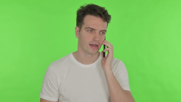 Молодой человек говорит по телефону на зеленом фоне — стоковое видео