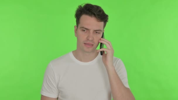 Irritado jovem homem falando no telefone no fundo verde — Vídeo de Stock