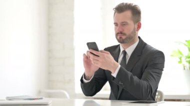 Ofiste akıllı telefon kullanan çekici genç iş adamı. 
