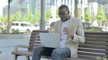 Afro-Amerikalı Adam, Bench 'te otururken dizüstü bilgisayarda kaybına tepki veriyor.