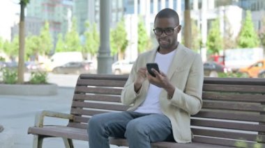Bench 'te otururken Smartphone' da Afrikalı Amerikalı Adam Online Başarı Kutlaması