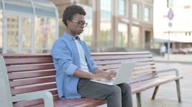 African Man with Headache Using Laptop while Sitting Outdoor on Bench