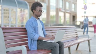 African Man with Laptop Smiling at Camera while Sitting Outdoor on Bench