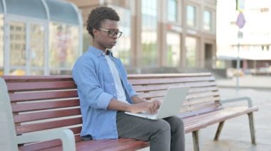 African Man with Back Pain Using Laptop while Sitting Outdoor on Bench