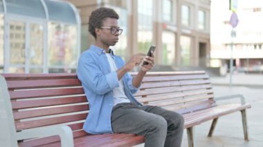 Afrikalı Adam Smartphone 'da internette gezinirken Bench' te oturuyor.
