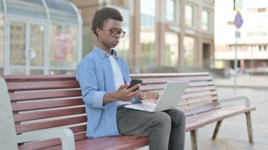 African Man Using Smartphone and Laptop while Sitting Outdoor on Bench
