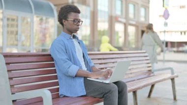Coughing African Man Using Laptop while Sitting Outdoor on Bench