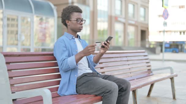 Aufgeregter Afrikaner Kauft Online Smartphone Ein Während Draußen Auf Bank — Stockvideo