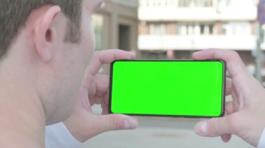 Close Up of Casual Man Holding Horizontal Smartphone with Green Screen Outdoor