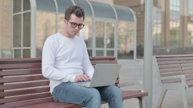 Casual Man with Laptop Smiling at Camera while Sitting Outdoor on Bench
