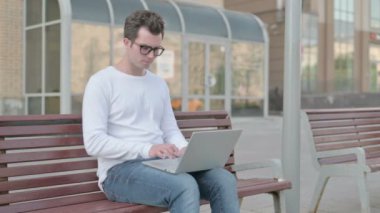 Casual Man with Wrist Pain Using Laptop while Sitting on Bench