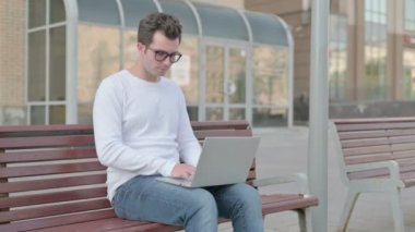 Casual Man with Laptop Showing Thumbs Up Sign While Sitting Outdoor on Bench 