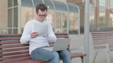 Casual Man Celebrating Success while Reading Documents and Working on Laptop Outdoor