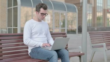Casual Man with Headache Using Laptop while Sitting Outdoor on Bench