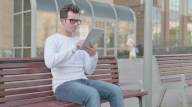 Casual Man using Tablet while Sitting Outdoor on Bench