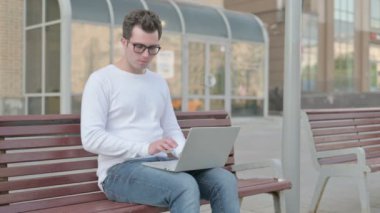 Casual Man with Neck Pain Using Laptop while Sitting Outdoor on Bench