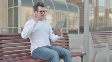 Online Video Chat on Tablet by Casual Man Sitting Outdoor on Bench 