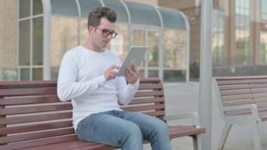 Casual Man Reacting to Loss on Tablet while Sitting Outdoor on Bench