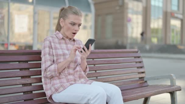 Casual Woman Celebrating Online Success Smartphone While Sitting Outdoor Bench — Stock video