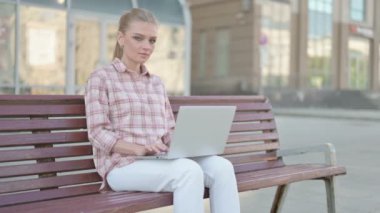 Casual Woman with Laptop Smiling at Camera while Sitting Outdoor on Bench