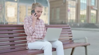 Casual Woman Talking on Phone and using Laptop while Sitting Outdoor on Bench
