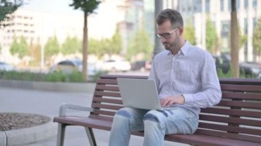 Rejecting Adult Man in Denial While using Laptop Sitting Outdoor on Bench 