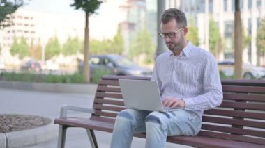 Thumbs Down by Adult Man with Laptop Sitting on Bench 