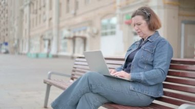 Senior Old Woman with Neck Pain Using Laptop while Sitting Outdoor on Bench