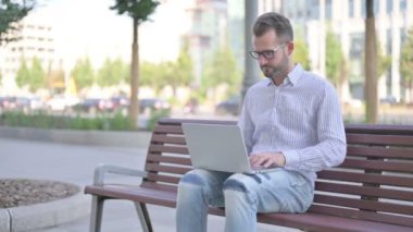 Adult Man Celebrating Success on Laptop while Sitting Outdoor on Bench