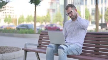 Adult Man with Neck Pain Using Laptop while Sitting Outdoor on Bench