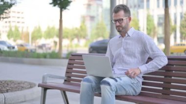 Adult Man with Back Pain Using Laptop while Sitting Outdoor on Bench