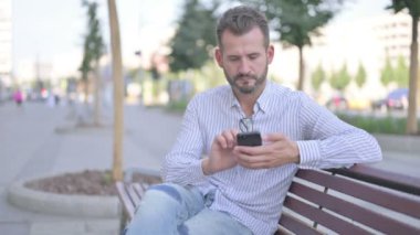 Adult Man Using Smartphone while Relaxing on Bench