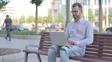Busy Adult Man Using Laptop Sitting Outdoor on Bench