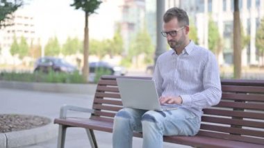 Adult Man with Headache Using Laptop while Sitting Outdoor on Bench