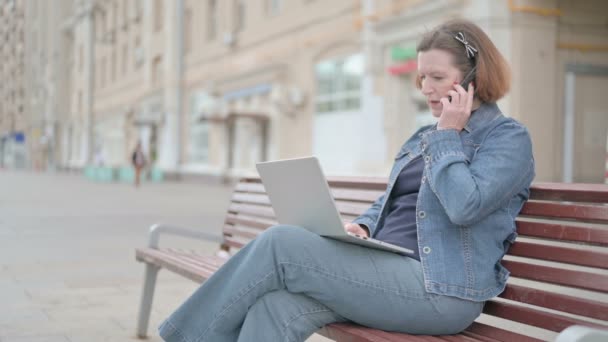 Senior Old Woman Talking Phone Using Laptop While Sitting Outdoor — Vídeos de Stock