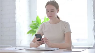Young Woman Browsing Internet on Smartphone in Office 