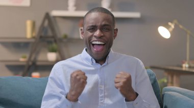 The Portrait of Young African Man Celebrating Success while Sitting on Sofa