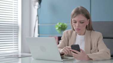 Ofiste dizüstü bilgisayar kullanırken Smartphone kullanan genç iş kadını