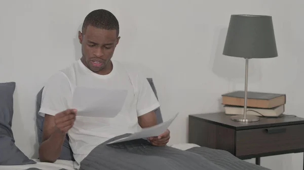 Young African Man Reading Reports While Sitting Bed — 스톡 사진