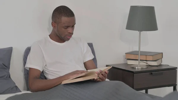 The Young African Man Reading Book while Sitting in Bed