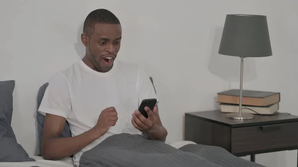 Young African Man Celebrating Success Smartphone Sitting Bed — Fotografia de Stock