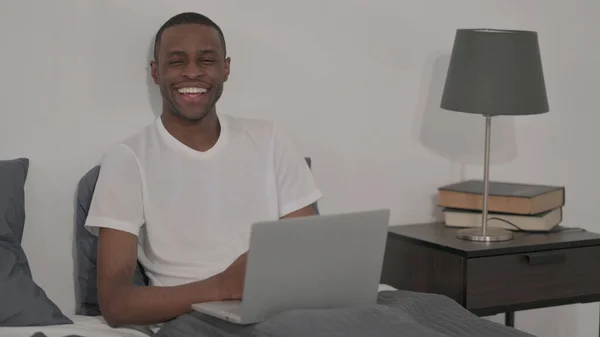 Young African Man Smiling Camera While Using Laptop Bed — 스톡 사진