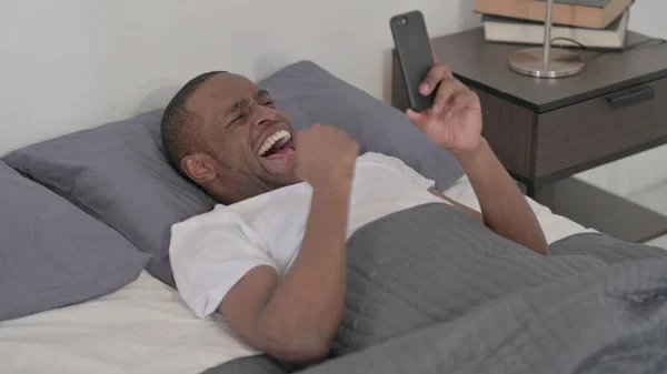 Young African Man Celebrating Success Smartphone Bed — Fotografia de Stock